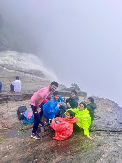 A group of friends sitting at the edge of the Bandaje waterfalls, with the powerful cascade of water right beside them.