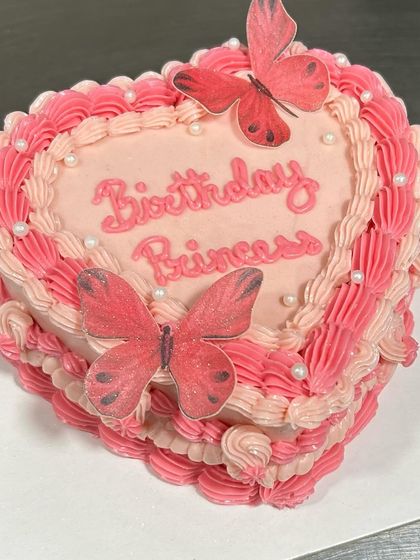 This heart-shaped "Birthday Princess" cake is adorned with delicate piping and edible butterflies. It's a dreamy cake for a special celebration.