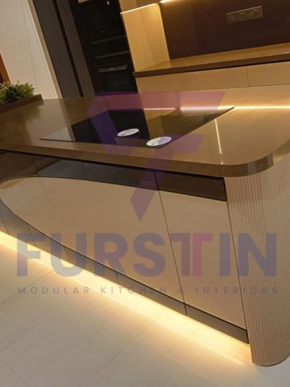 A close-up of the curved kitchen island, a detail that softens the modern aesthetic. The integrated induction cooktop and subtle profile lighting along the base demonstrate our attention to both design and practicality.