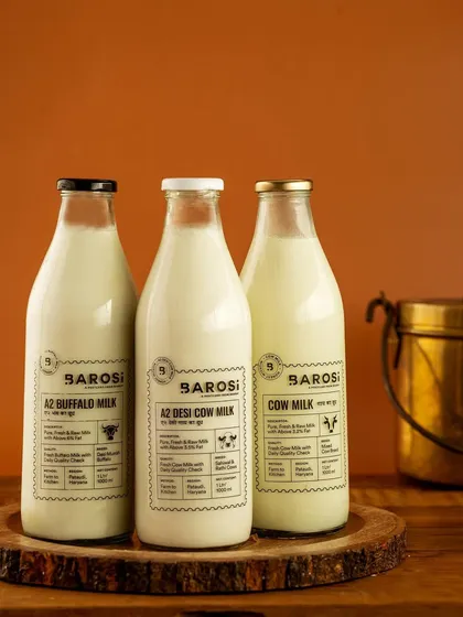 A clean product shot of Barosi's three types of milk bottles. The simple wooden backdrop and warm lighting give a rustic yet premium feel, focusing on the clean packaging and farm-fresh promise.