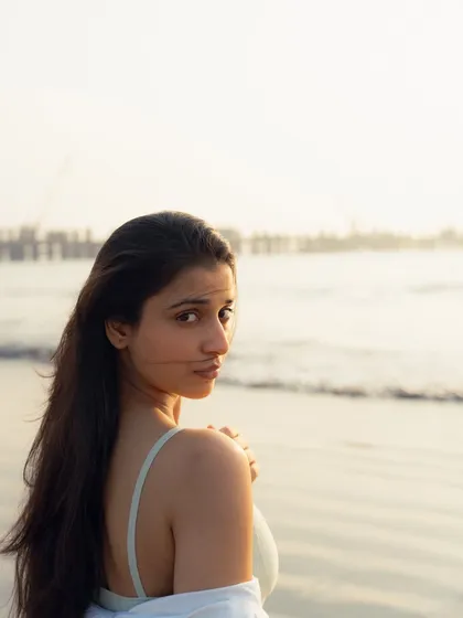 An intimate, over-the-shoulder glance that creates a direct connection with the viewer. The soft focus on the sea behind her adds depth.