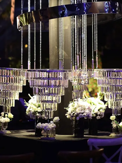 A modern, multi-tiered crystal chandelier centerpiece, surrounded by small bouquets of white flowers.