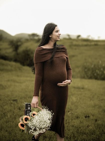 A lovely solo portrait of the mom-to-be walking through a field, holding a basket of flowers and sonogram pictures, looking off into the distance with a hopeful expression.