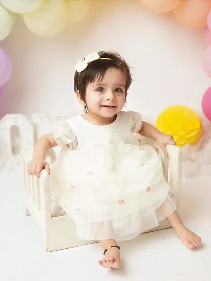 A beautiful, bright smile from the one-year-old. The pastel rainbow balloon arch creates a cheerful and celebratory backdrop for her first birthday photos.
