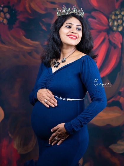 A regal portrait against a painted floral backdrop. The mom-to-be wears a classic navy blue gown and a crown, exuding confidence and grace.