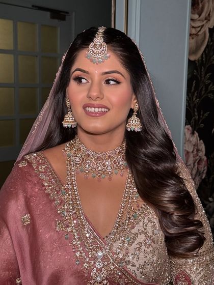 A beautiful bride with her hair styled in soft waves, tucked behind one ear to show off her stunning earrings. A maang tikka completes this classic bridal look.