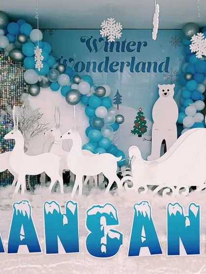 A magical Winter Wonderland theme for a joint birthday party. This setup includes white reindeer cutouts, a snowman, a sleigh, and a blue and silver balloon arch to create a snowy scene.