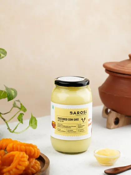 A jar of Cultured Cow Ghee styled with traditional Indian sweets (jalebi) and an earthen pot, connecting the product to festive indulgence.