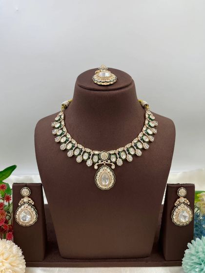 The Amaya Premium Moissanite Kundan Necklace. This set is distinguished by its large central pendant and matching earrings, featuring fine Meenakari work. It is available with red or green accents.