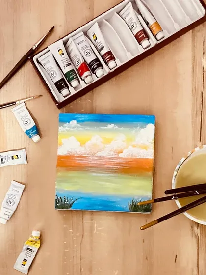 Sometimes I just need to paint for myself. Here's a small canvas painting of a serene sunset over the water, surrounded by my paints and brushes.