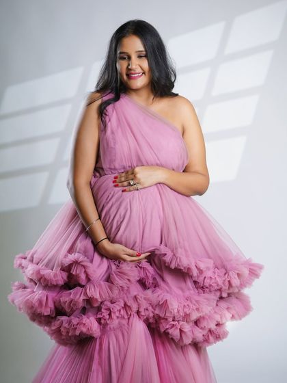 A close-up portrait focusing on the mother lovingly holding her bump. The texture of the pink gown adds a soft and romantic feel to the photograph.