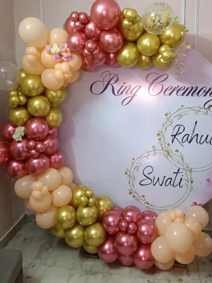 For your engagement or ring ceremony, I can create a personalized backdrop like this one. It features a custom-printed circular board with the couple's names, framed by a beautiful organic balloon arch in shades of rose, gold, and peach for a perfect photo opportunity.