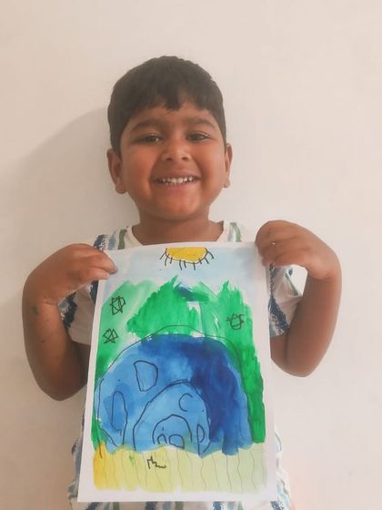 A young boy smiles as he holds his colorful painting of a mother and baby elephant under a bright sun.