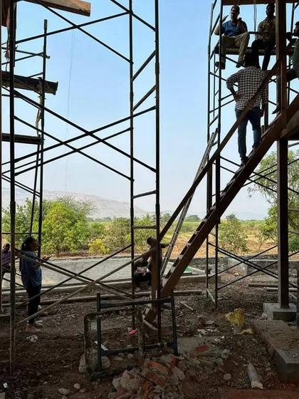 A view from inside the farmhouse looking out, with the team working on the roof. The scaffolding becomes a temporary part of the architecture, a necessary framework for the craftspeople to do their work.