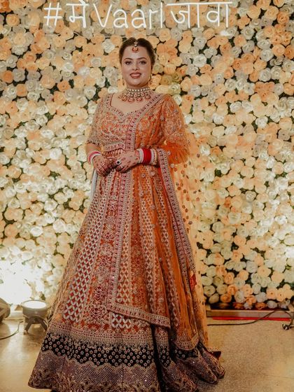 A happy client looking radiant in her wedding lehenga against a flower wall. Seeing my clients this happy is the best reward.