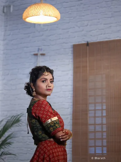 A wider shot of a model in a traditional printed lehenga, showing the indoor setting. The composition uses the interior elements like the bamboo blinds and overhead light to frame the shot.