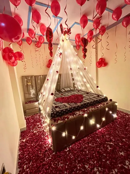 I create truly romantic and memorable experiences. This bedroom decoration features a beautiful canopy with fairy lights, hundreds of red balloons, and a floor covered in rose petals for the perfect surprise.