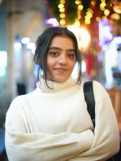 A confident and relaxed pose with arms crossed. The blurred lights in the background create a beautiful contrast with her white sweater, making the portrait stand out.