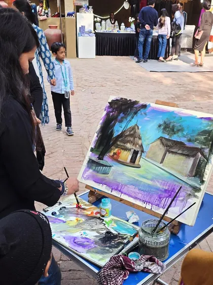 An artist at her easel during our outdoor session, painting a rustic hut scene with acrylics amidst the inspiring surroundings of the Craft Museum.
