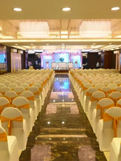 The beautiful interior of Ellora Banquet hall, featuring elegant chandeliers and a long aisle leading to the stage. The seating is arranged neatly with white and yellow covers.