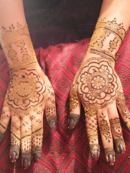 A beautiful mandala design on the back of the hands, featuring a floral center and delicate, web-like patterns on the fingers. The dark-tipped fingers add a traditional touch.