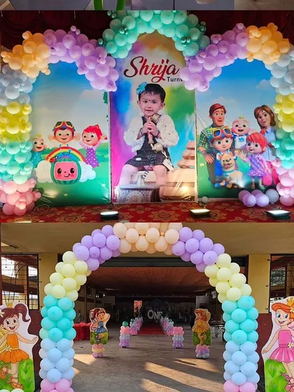 A large-scale Cocomelon entrance decoration featuring two balloon arches and a backdrop personalized with the birthday girl's photo.