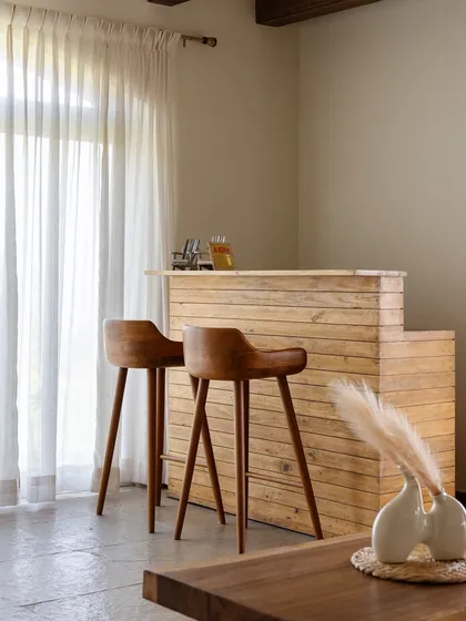 The bar area is crafted from reclaimed wood, continuing the villa's earthy and sustainable theme. Simple, elegant bar stools and sheer curtains create a light and airy space for casual entertaining.
