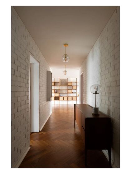 The main hallway, lined with whitewashed brick, leads the eye towards the open-plan living area, with the warm teak floor providing a sense of direction.