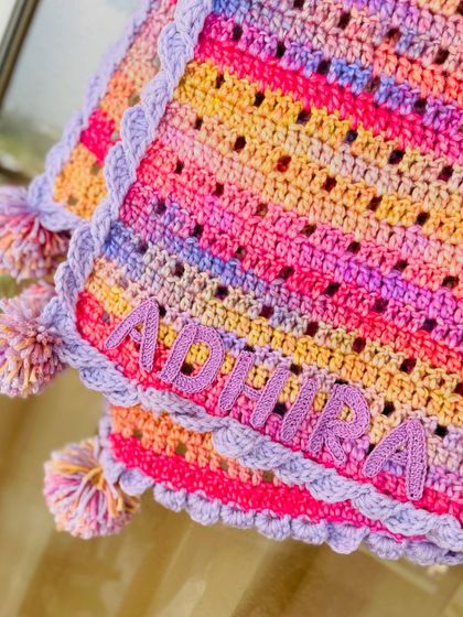 A close up of the name "Adhira" crocheted onto the blanket. We take great care to make the lettering neat and secure, ensuring it becomes a lasting part of this handmade treasure.