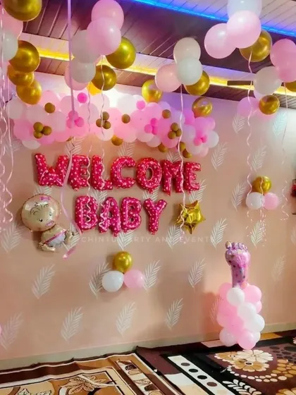 A 'Welcome Baby' decoration for a baby girl's arrival at home. The setup uses pink and gold balloons and large foil letters.