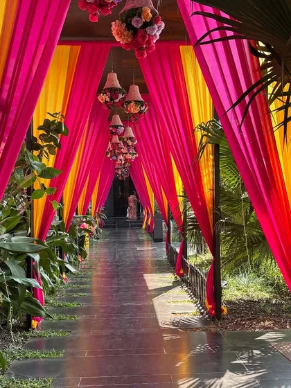 We created a grand and colorful entrance for this Mehendi ceremony. The long walkway was lined with lush greenery and covered with bright pink and yellow drapes, with hanging chandeliers adding a touch of elegance.
