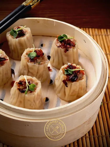 A bamboo steamer filled with savory siu mai dumplings, garnished with microgreens. A classic dim sum offering that is always a guest favorite.