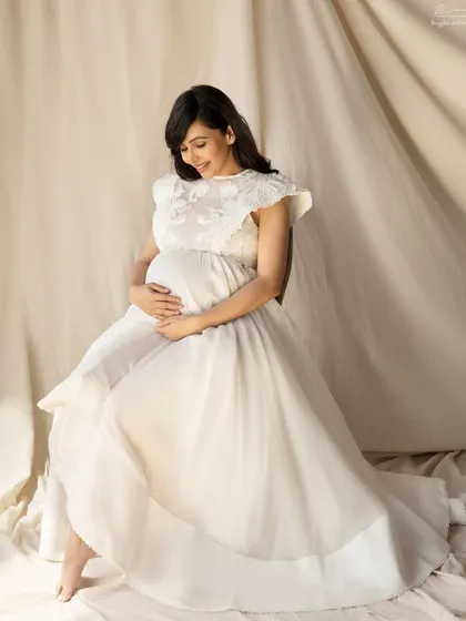 A vintage-inspired white dress creates a feeling of timeless grace. This seated portrait is serene and beautiful, focusing on the quiet bond with your baby.