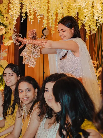 A close-up of the bride shaking her kaleerein over her friends. I ensure the photographers are ready to capture the expressions of hope and excitement.