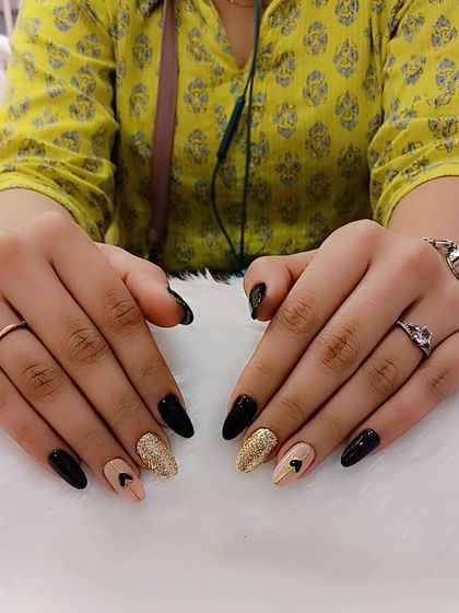Black nails, endless attitude. Ready to slay the day (or night) with this chic combination of glossy black, sparkling gold glitter, and nude accent nails with tiny hearts.