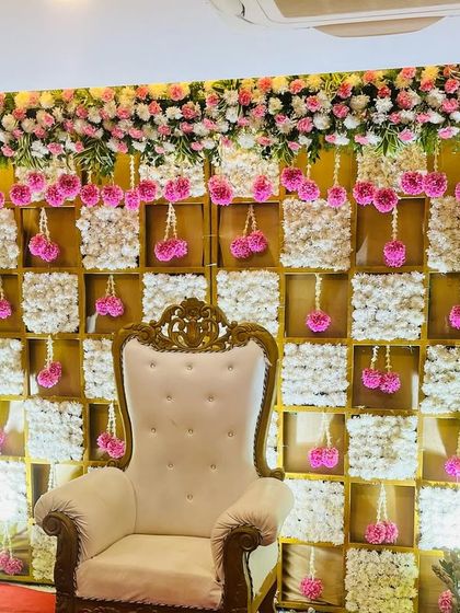 A lovely pink and white themed backdrop for a baby shower. The checkerboard design is made with panels of white flowers, accented by hanging pink floral tassels for a delicate and feminine touch.