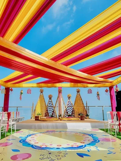 A vibrant Haldi ceremony set against a stunning seaside backdrop. We used bright yellow and pink fabric drapes to create a festive canopy, with a custom-printed floor and floral arrangements that make for incredible photos and an even better experience.