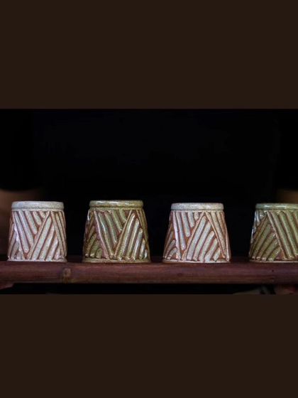 A set of four KHUMĀR shot glasses on a wooden platter. They carry the same carved texture as the mugs, making them a perfect addition to your barware.