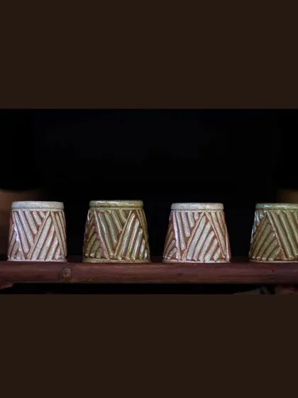 A set of four KHUMĀR shot glasses on a wooden platter. They carry the same carved texture as the mugs, making them a perfect addition to your barware.