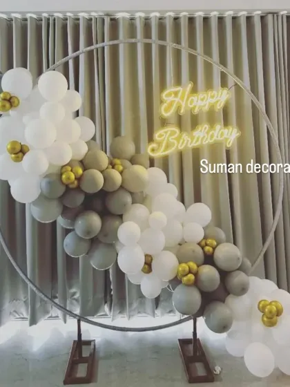 A minimalist and modern birthday setup with a balloon garland in grey, white, and gold on a simple ring frame. The "Happy Birthday" neon sign adds a warm glow.