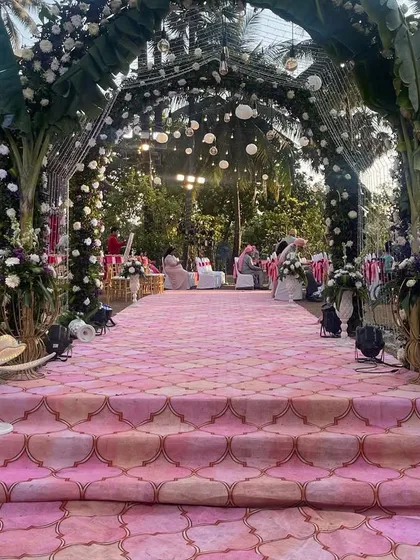 A beautiful pink-themed aisle leading up to a mandap decorated with banana leaves and florals. The lotus-shaped floor lamps add a unique and elegant touch to the pathway.
