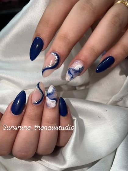 A sophisticated design in navy blue. This set includes solid blue nails, a marble accent nail, and a glittery swirl design.