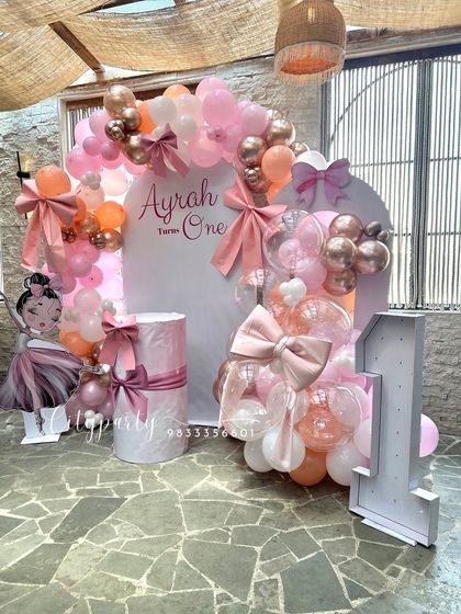 A full view of the bow-themed first birthday, showing the combination of the balloon arch, custom backdrop, and light-up number '1'.