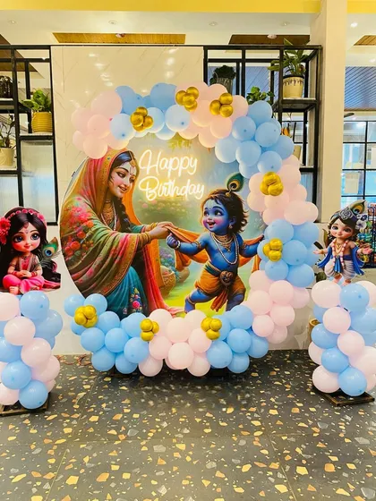 A custom Krishna-themed decoration featuring a circular backdrop with traditional artwork and a surrounding balloon arrangement. This setup is a popular choice for a baby's naming ceremony or first birthday party.