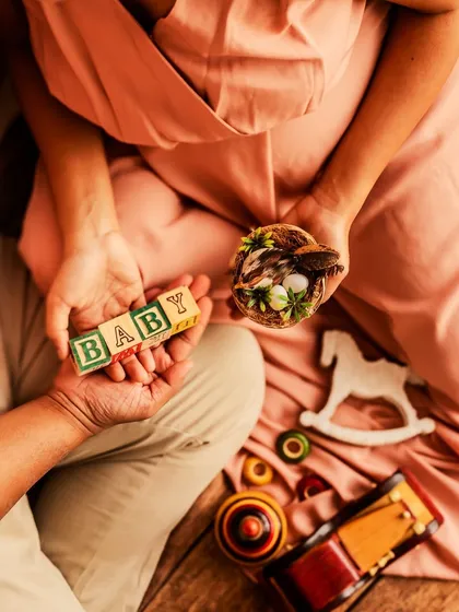 A detailed flat-lay style shot focusing on the hands of the couple holding baby blocks and a tiny nest. This artistic composition is rich with symbolism about building a home and nurturing new life.