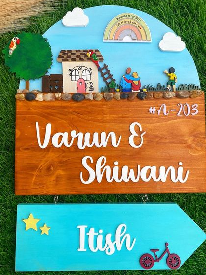 This nameplate tells the story of a growing family. The main plaque features the couple, while a separate arrow-shaped sign points the way for their little one. The hand-painted sky, rainbow, and miniature details make this a truly magical piece.