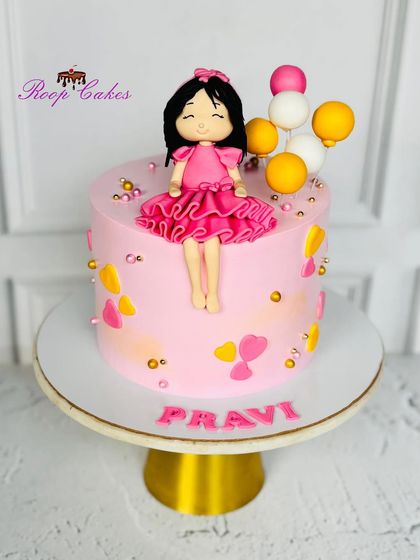 A pretty pink cake for a little girl named Pravi. The design is decorated with yellow and pink hearts and topped with a handcrafted fondant doll and a bunch of balloons.