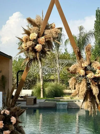 A stunning triangular arch decorated with dried florals and pampas grass stands by the pool, serving as a perfect photo spot for this boho-chic baby shower.