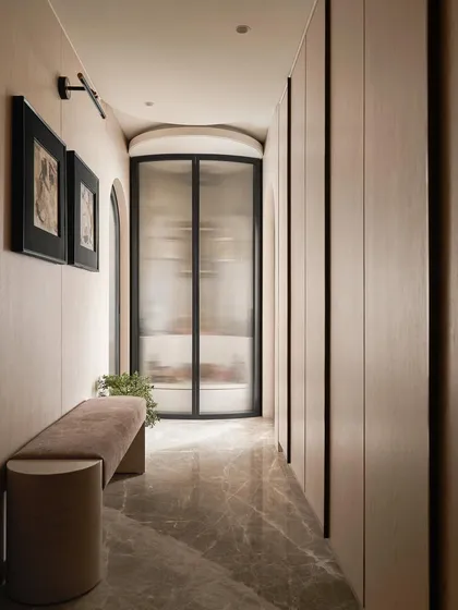 The entrance to this master bedroom is a long passage lined with custom, full-height wardrobes. By designing them to be flush with the walls and using a consistent light wood veneer, the storage becomes an integrated architectural element rather than bulky furniture.