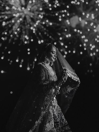 A black and white portrait of the bride against a backdrop of fireworks. The dramatic lighting and her elegant pose create a celebratory and timeless image.